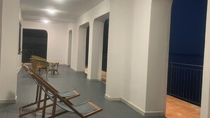 Um corredor com paredes brancas, piso escuro e cadeiras de madeira.