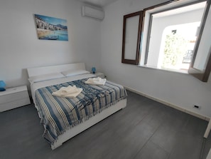 Ein Schlafzimmer mit einem Bett, einem Nachttisch, einer Lampe, einem Gemälde und einem Fenster.
