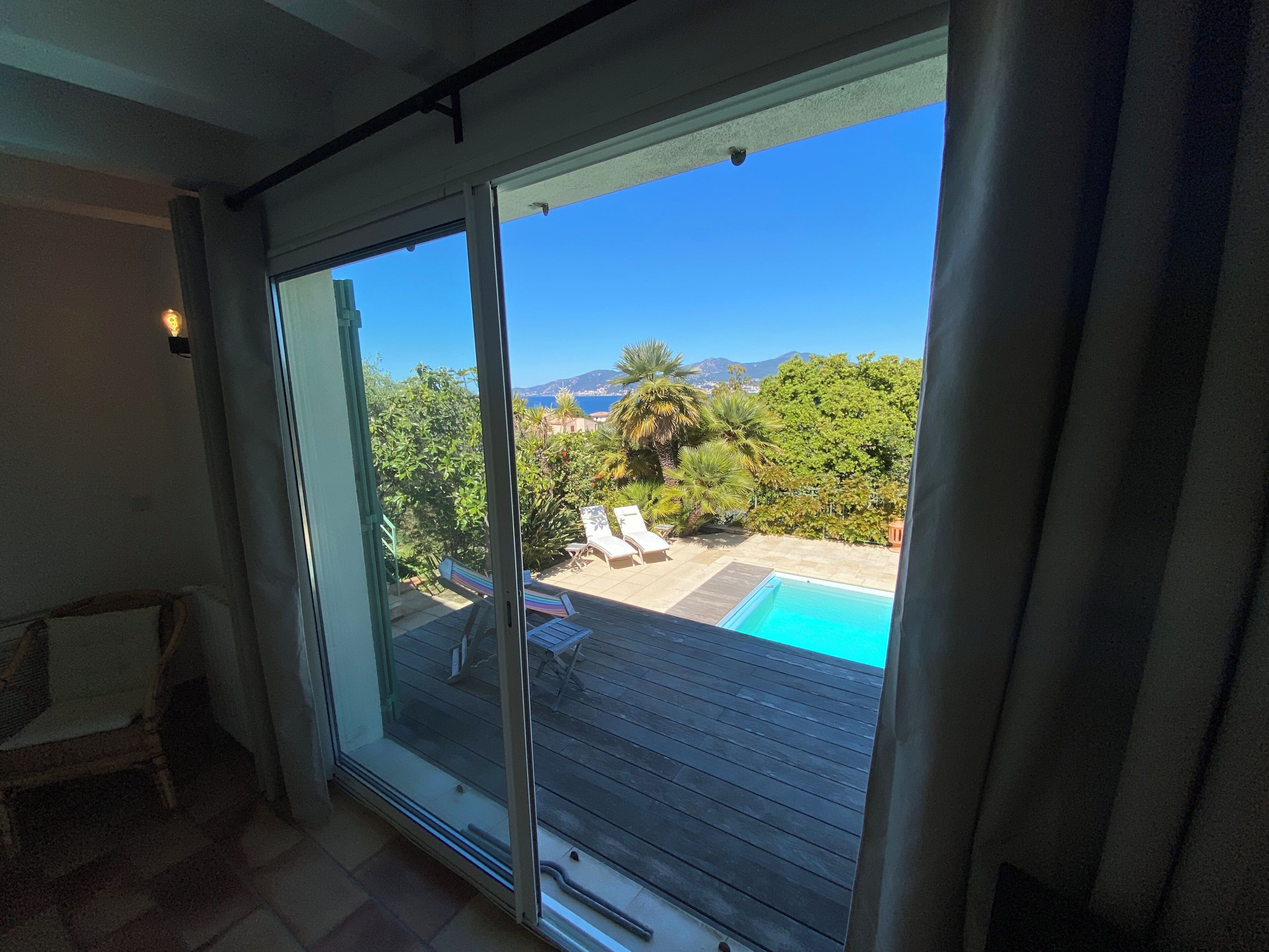 Une pièce dotée d’une porte-fenêtre coulissante donnant sur un espace extérieur avec une piscine et des chaises longues.