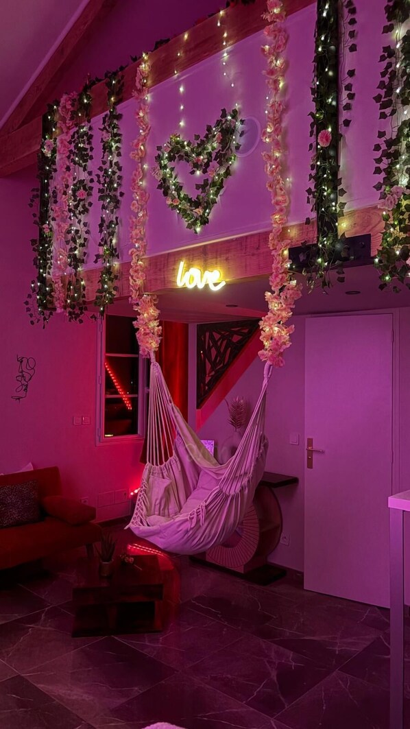 Une pièce avec un hamac, un néon en forme de cœur sur lequel est écrit le mot « amour », et des décorations en forme de cœur.
