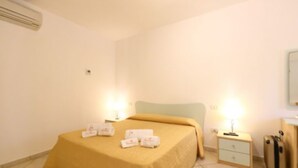A hotel room with a bed, bedside tables, a nightstand, a lamp, and a suitcase. - Studio for Couples in Capo Vaticano With Pool (Ricadi)
