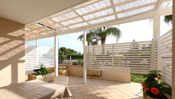 A covered patio area with a table and chairs, a pergola overhead, and a view of palm trees and greenery. - Studio for Couples in Capo Vaticano With Pool (Ricadi)