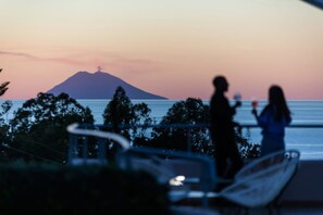 A view of a beach with a mountain in the background, a railing, and a person holding a drink. - Studio for Couples in Capo Vaticano With Pool (Ricadi)