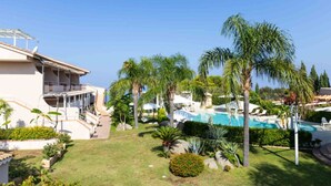 A resort with a swimming pool, palm trees, and a building with a covered outdoor area. - Studio for Couples in Capo Vaticano With Pool (Ricadi)