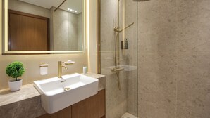 Een moderne badkamer met een witte wasbak, gouden details, een douche met glazen wanden en een kleine plant in pot.