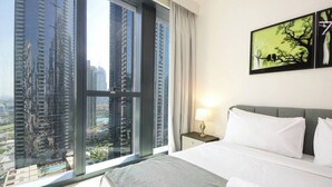 Hotelkamer met een groot bed, een nachtkastje, een lamp en uitzicht op hoge gebouwen door een groot raam.