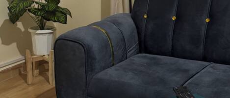 En mørkeblå sofa med guldknapper, et hvidt bord med marmorering, toiletpapir og en potteplante.