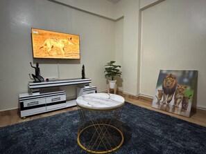 Olohuoneessa on taulutelevisio, moderni viihdekeskus, pyöreä sohvapöytä, ruukussa oleva kasvi ja leijonien kuva.