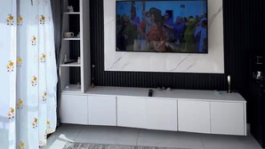 Ett modernt vardagsrum med en stor platt-TV som är monterad på en vit TV-möbel, en mönstrad matta och en taklampa.