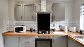 A modern kitchen with grey cabinets, a stainless steel range hood, a microwave, a stove, a toaster, and a sink. - Modern House In Hartlepool With Private Parking (Hartlepool)