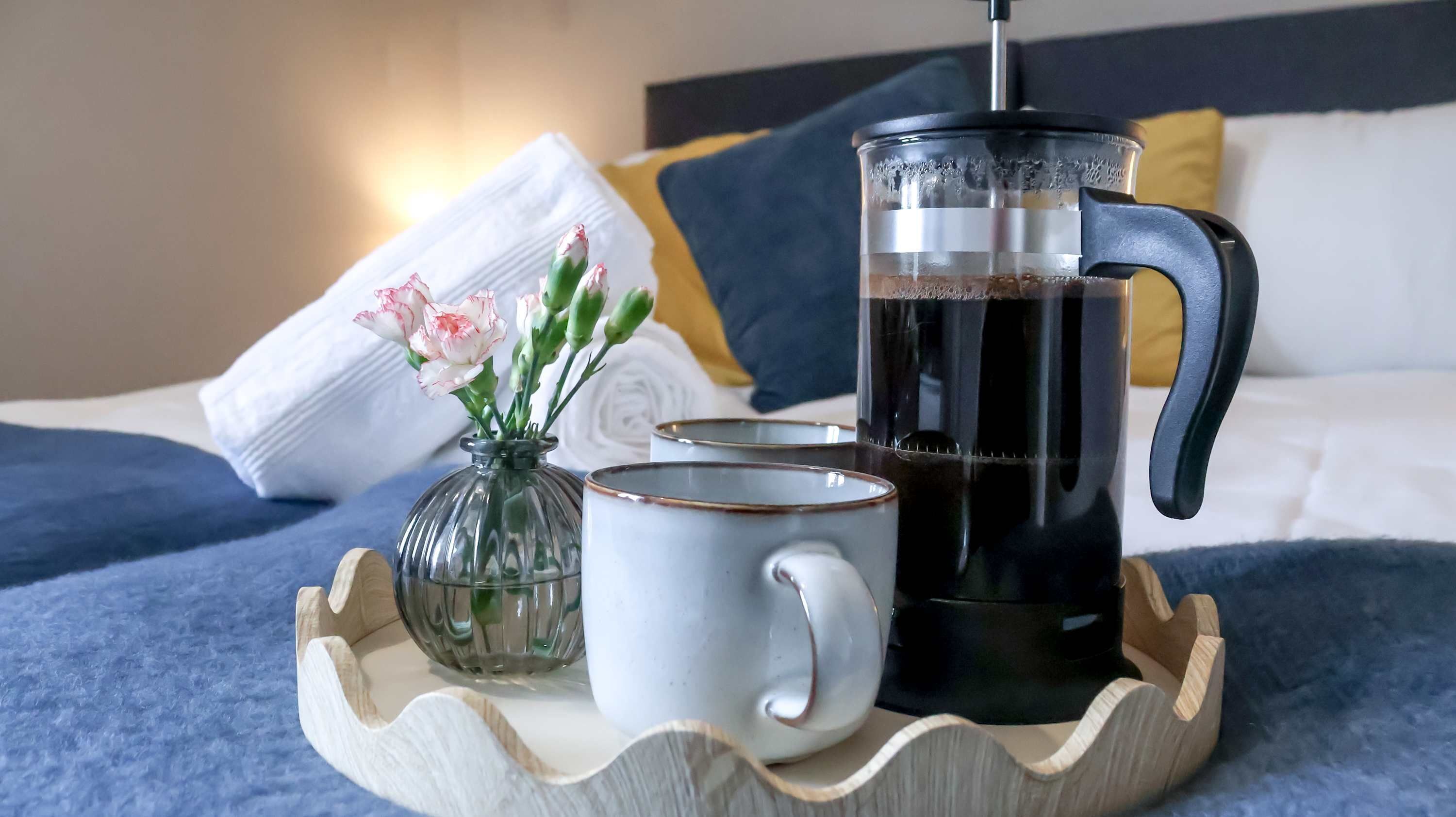A coffee maker, two cups, and a vase with flowers on a tray.