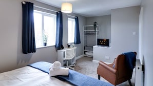 A hotel room with a bed, a chair, a desk, a TV, and a window with curtains. - Modern House In Hartlepool With Private Parking (Hartlepool)