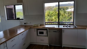 A kitchen with a wooden countertop, a built-in dishwasher, and a window with a view of greenery and buildings.