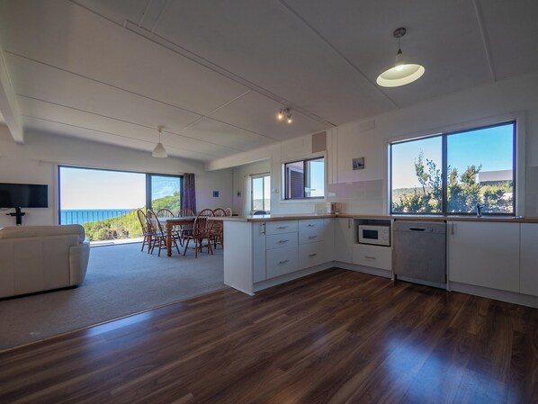 A modern kitchen with a dining area, large windows, and a view of the ocean.