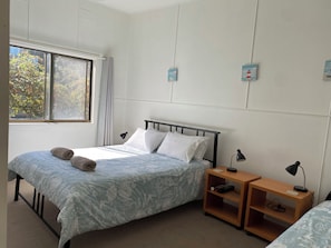 A bedroom with a bed, two bedside tables, a window, and a wall-mounted shelf.
