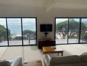 A spacious living room with a large sliding glass door leading to a balcony with a view of the ocean.