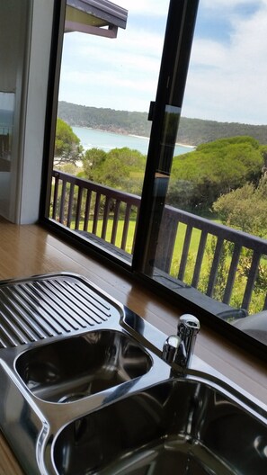 Una cocina con un lavamanos de acero inoxidable y vistas a un paisaje costero a través de amplios ventanales.