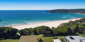 Paisaje costero con una playa, abundante vegetación y cielo despejado.