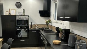 Une cuisine moderne avec des meubles de couleur noire, un four à micro-ondes, un four traditionnel et un évier. Il y a une fenêtre au-dessus de l’évier et une horloge au mur.