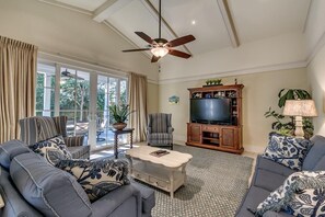Un salon avec un ventilateur de plafond, un téléviseur et une table basse.