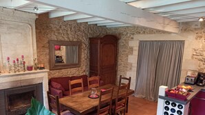 A dining area with a stone wall, wooden table, and chairs. A fireplace is visible on the left, and a wine rack is on the right. - Charming house with swimming pool near Saint Emilion (GARDEGAN ET TOURTIRAC)