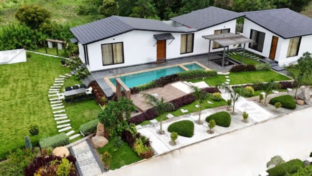 Une maison moderne à deux étages, dotée d’une piscine, entourée de pelouses et de jardins bien entretenus.