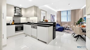 A modern kitchen with white cabinetry, a stainless steel range hood, and a black countertop. - WYZ RENT|Grand 1BR Cour Jardin Near Bay Avenue (Dubai)