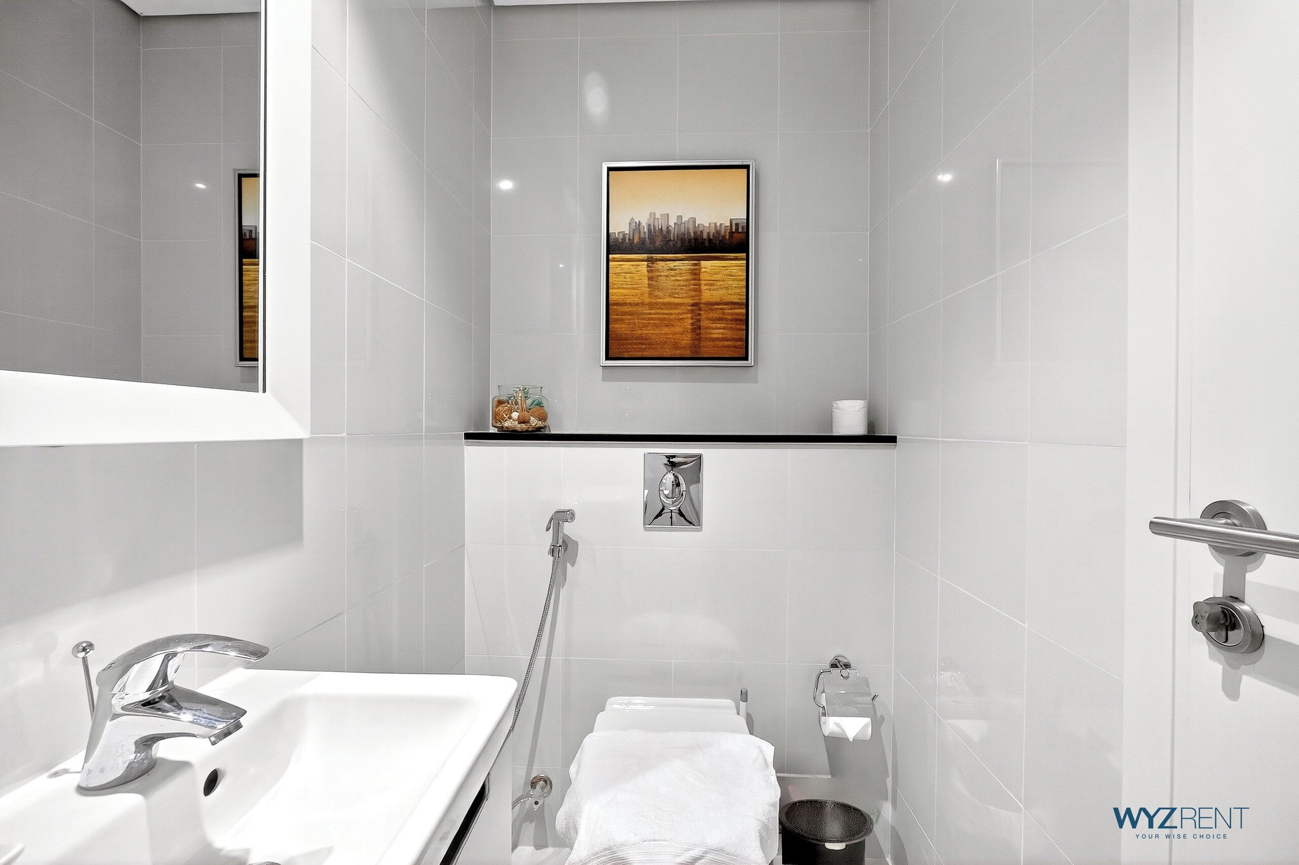 Een moderne badkamer met een witte wastafel, een handdouche, een handdoekrek en een stadsgezicht in een lijst aan de muur.