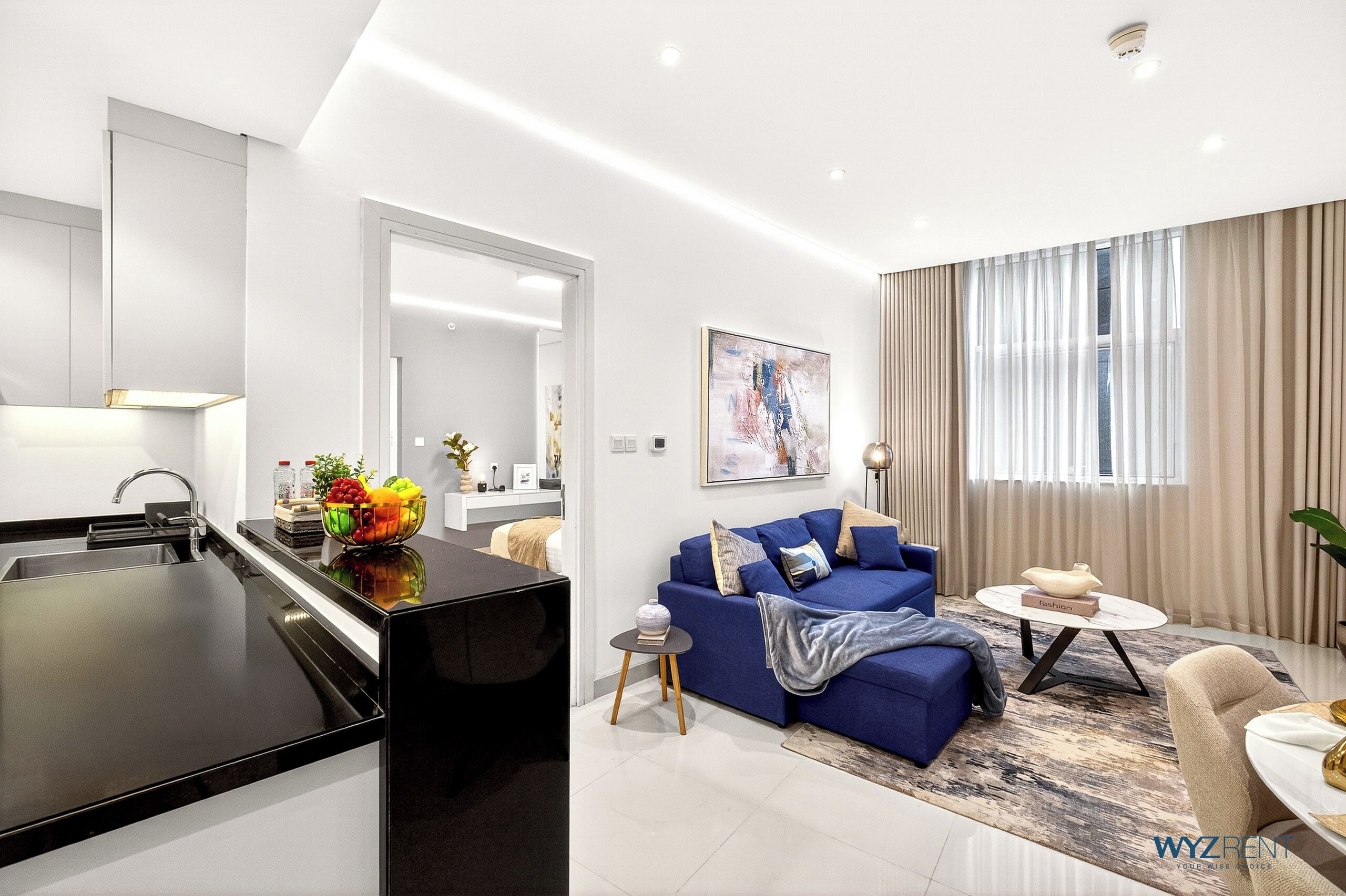 A modern living room with a blue sofa, a coffee table, and a kitchen area with a black countertop and sink.