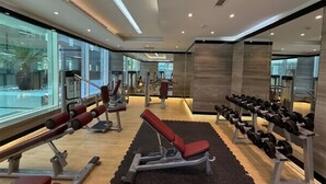 A modern gym with exercise equipment, large windows, and a wooden floor. - WYZ RENT|Grand 1BR Cour Jardin Near Bay Avenue (Dubai)