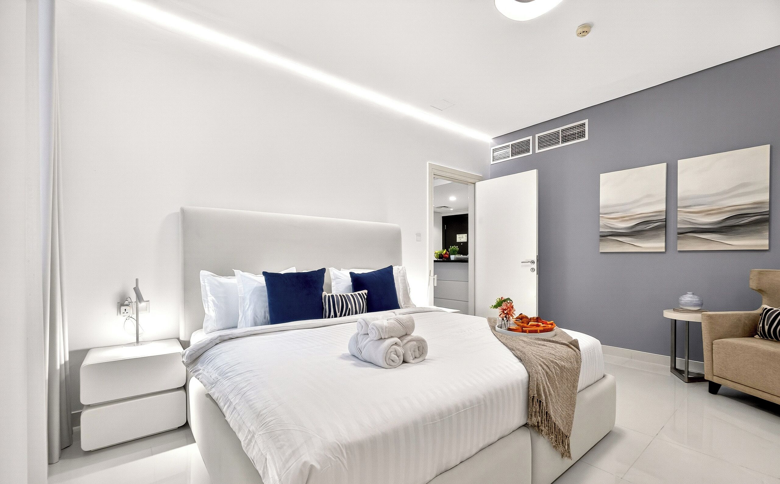 A modern bedroom with a large bed, bedside tables, a wardrobe, and artwork on the walls.