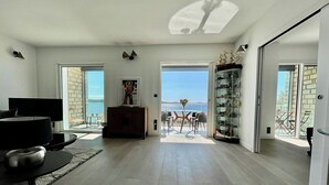 Ein geräumiger Wohnbereich mit großem Fenster, einem Flachbildfernseher, einem Holztisch und einer Glasvitrine.