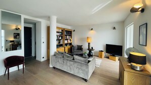Ein modernes Wohnzimmer mit grauem Sofa, Holzregalen, einem Fernseher und einem Holzschrank.