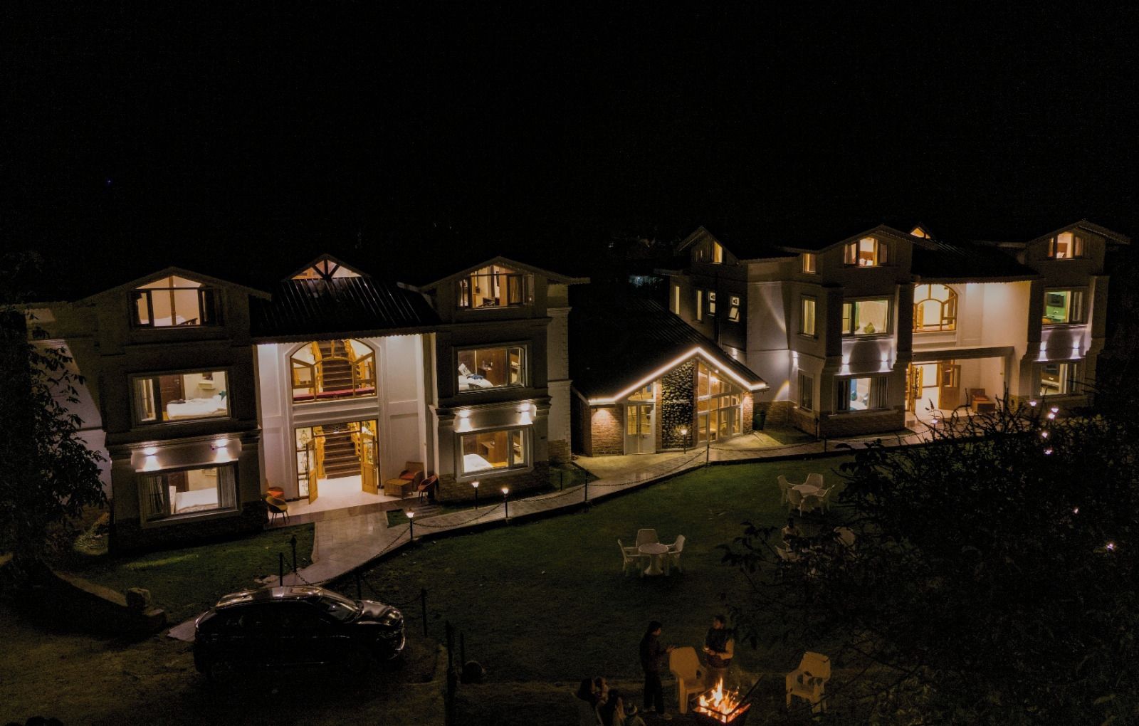 A multi-story residential building with a well-lit exterior, a visible staircase, and a fire pit area.