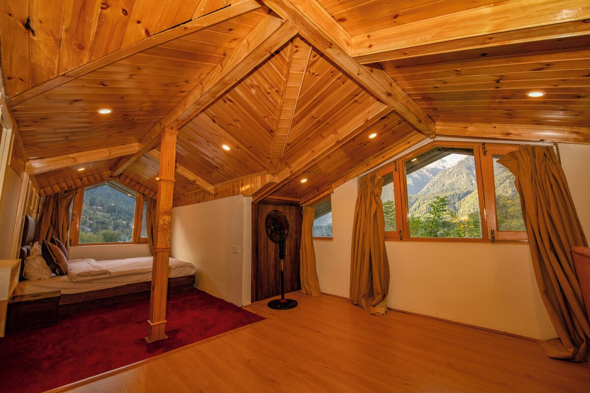 Una habitación con vigas de madera en el techo, una cama, un ventilador de pie y ventanas con cortinas.