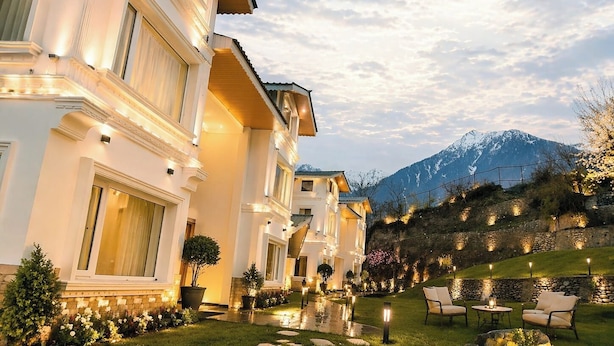 A multi-story hotel with a well-lit exterior, a landscaped garden with seating, and a mountain backdrop. - The Riviera Hotel Pahalgam (Pahalgam)