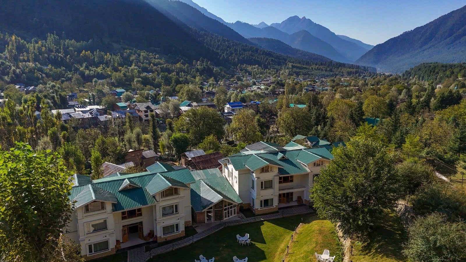 A multi-story building with a green roof, surrounded by lush greenery and mountains in the background.