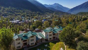 A multi-story building with a green roof, surrounded by lush greenery and mountains in the background.