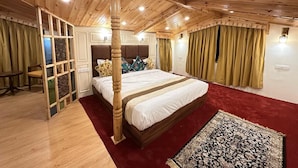 A bedroom with a wooden ceiling, a bed with white bedding, a red carpet, and a patterned rug. - The Riviera Hotel Pahalgam (Pahalgam)