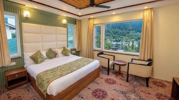 A hotel room with a large bed, a small table, a chair, and a view of a forest through the window.
