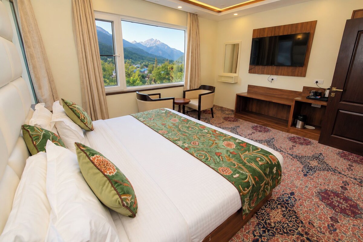 Habitación de hotel con una cama grande, un escritorio, un televisor y vistas a las montañas.