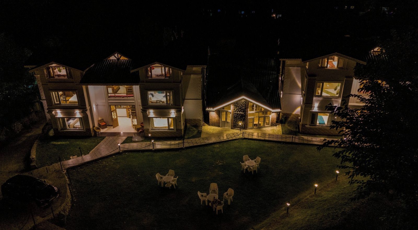 A multi-story hotel with a well-lit entrance, outdoor seating area, and a manicured lawn.