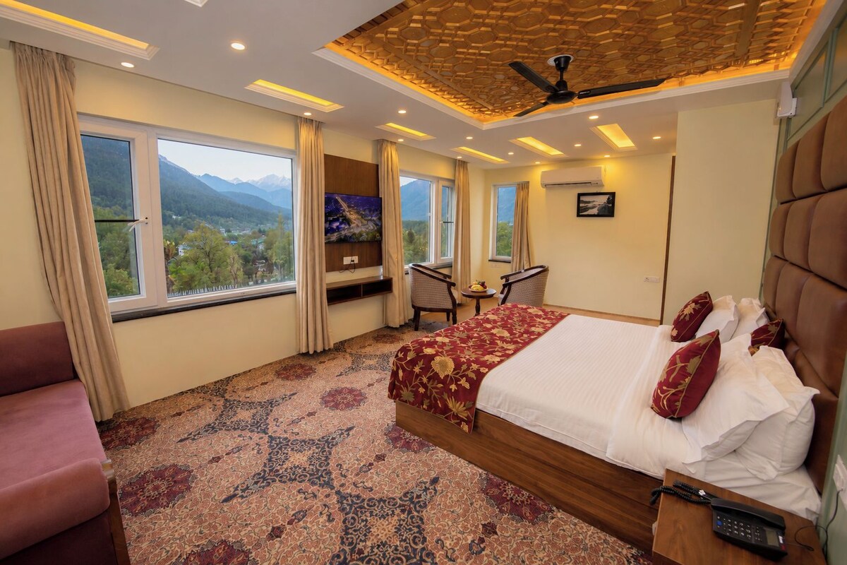 Habitación de hotel con una cama grande, un escritorio, una silla y vistas a las montañas.