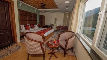 A hotel room with a large bed, two armchairs, a small table with drinks, and a view of the outdoors.