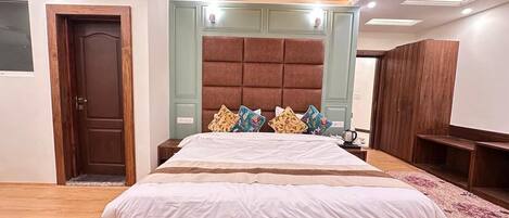 Un dormitorio con cama de madera, ventilador de techo, cabecera acolchada grande y alfombra estampada.