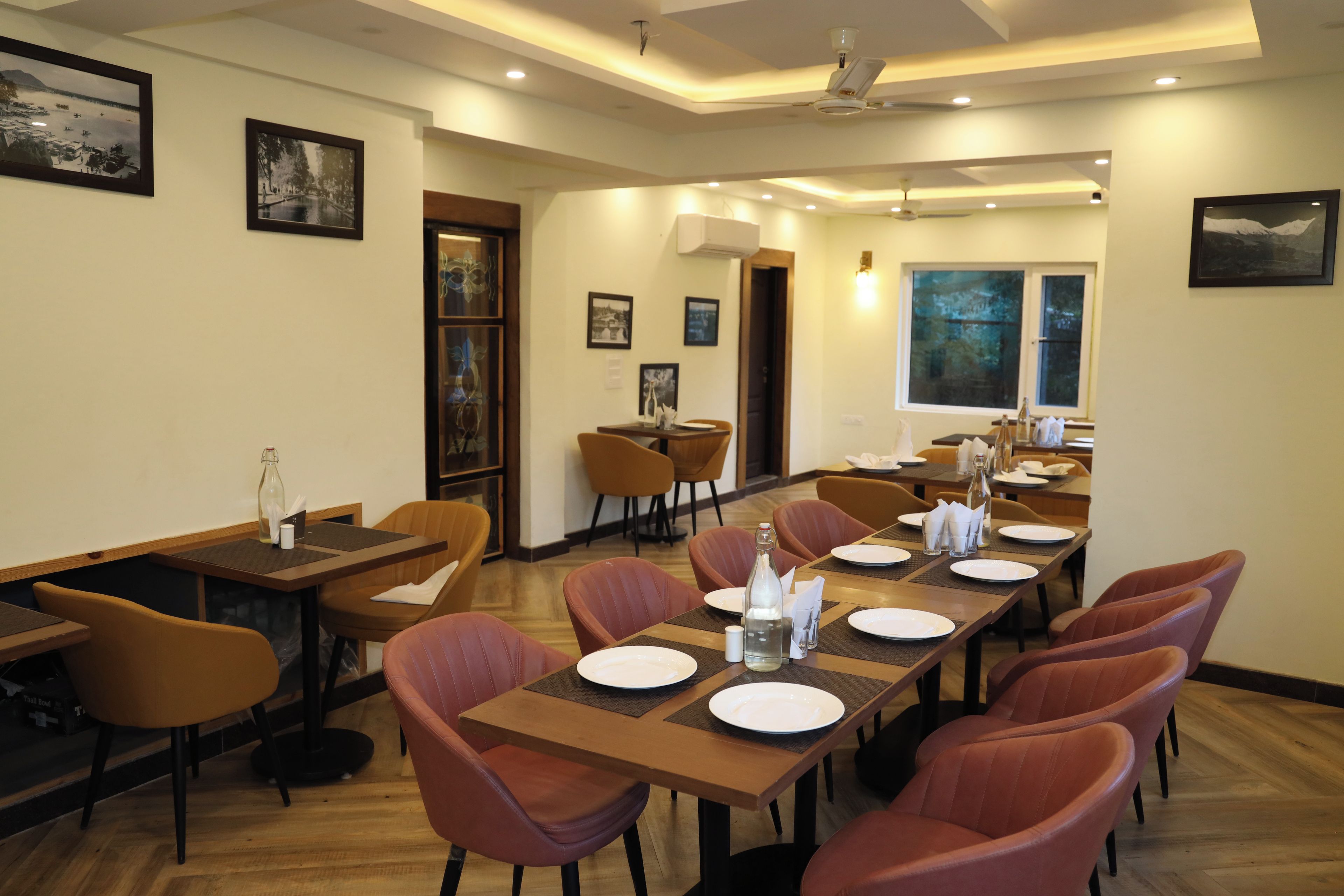 A conference room with wooden tables and chairs, framed pictures on the walls, and a large window with a view.