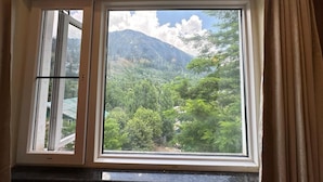 A window with a view of a mountainous landscape and dense greenery. - The Riviera Hotel Pahalgam (Pahalgam)