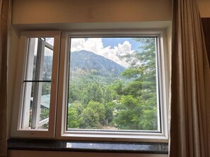 A window with a view of a mountainous landscape and dense greenery. - The Riviera Hotel Pahalgam (Pahalgam)