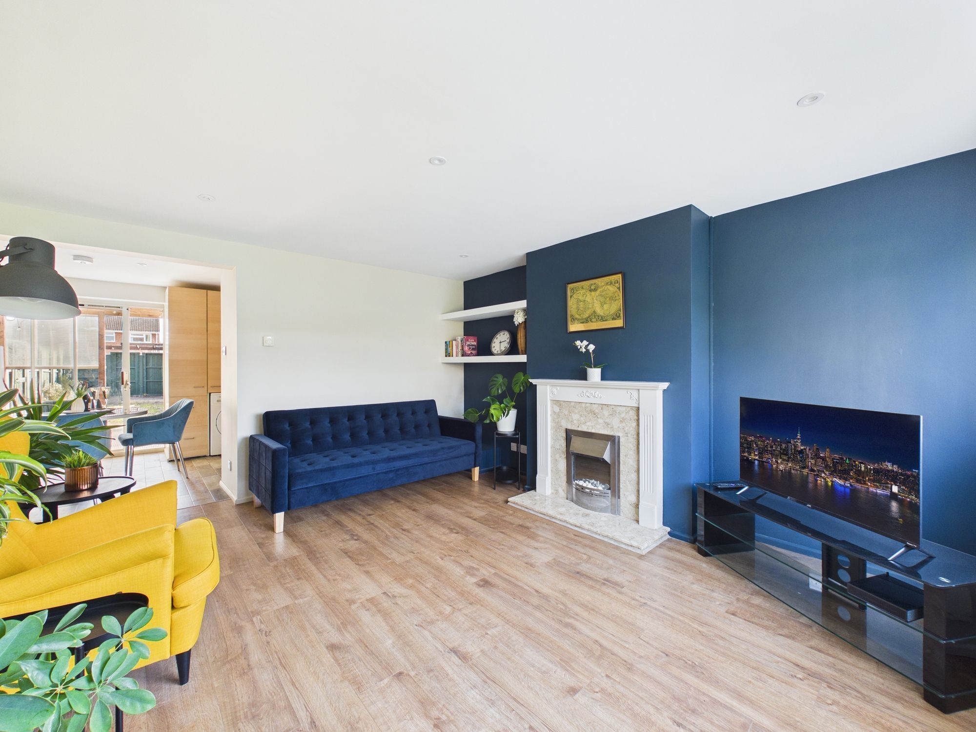A modern living room with a blue sofa, a yellow armchair, a fireplace, and a TV.