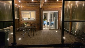 An outdoor patio area with a table and chairs, a wooden deck, and a glass door leading to an interior space with a table and chairs.